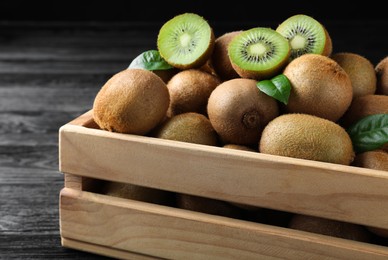 Crate with cut and whole fresh kiwis on black wooden table, closeup