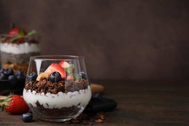 Photo of Tasty granola with berries, nuts and yogurt in glass on wooden table, space for text