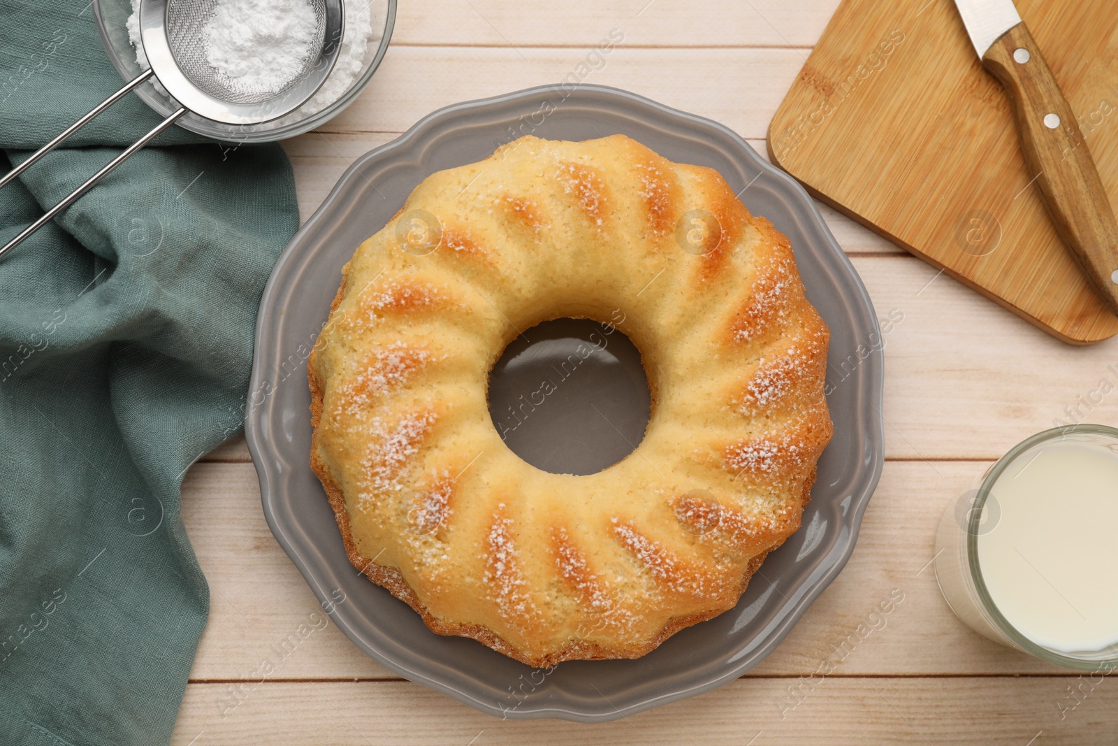 Photo of Delicious sponge cake with powdered sugar and glass of milk on wooden table, flat lay