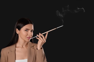 Photo of Woman using long cigarette holder for smoking on black background, space for text