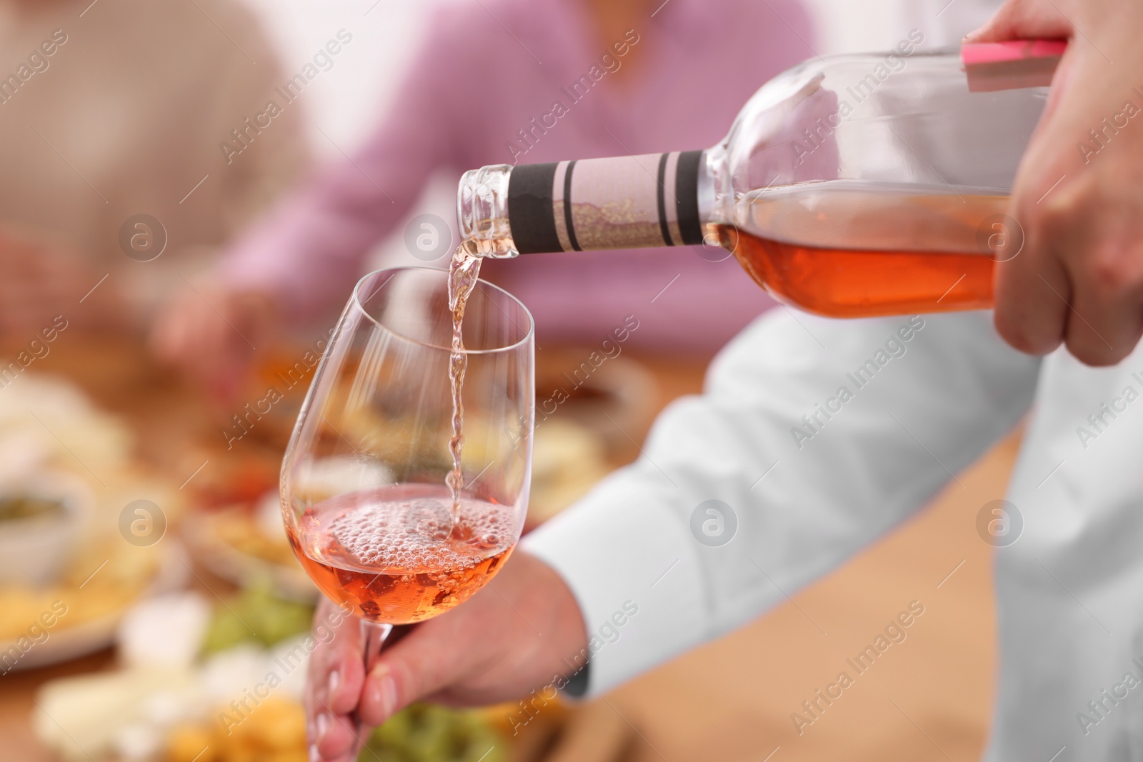 Photo of Man pouring rose wine from bottle into glass indoors, closeup