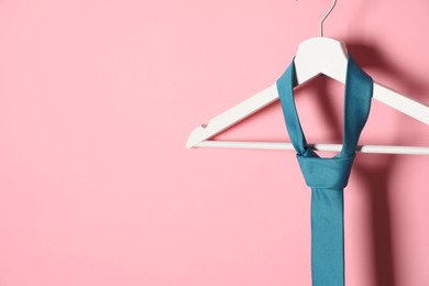 Photo of Hanger with turquoise tie on pink background. Space for text