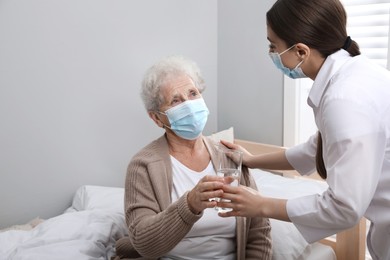 Doctor giving water to senior woman with protective mask at nursing home