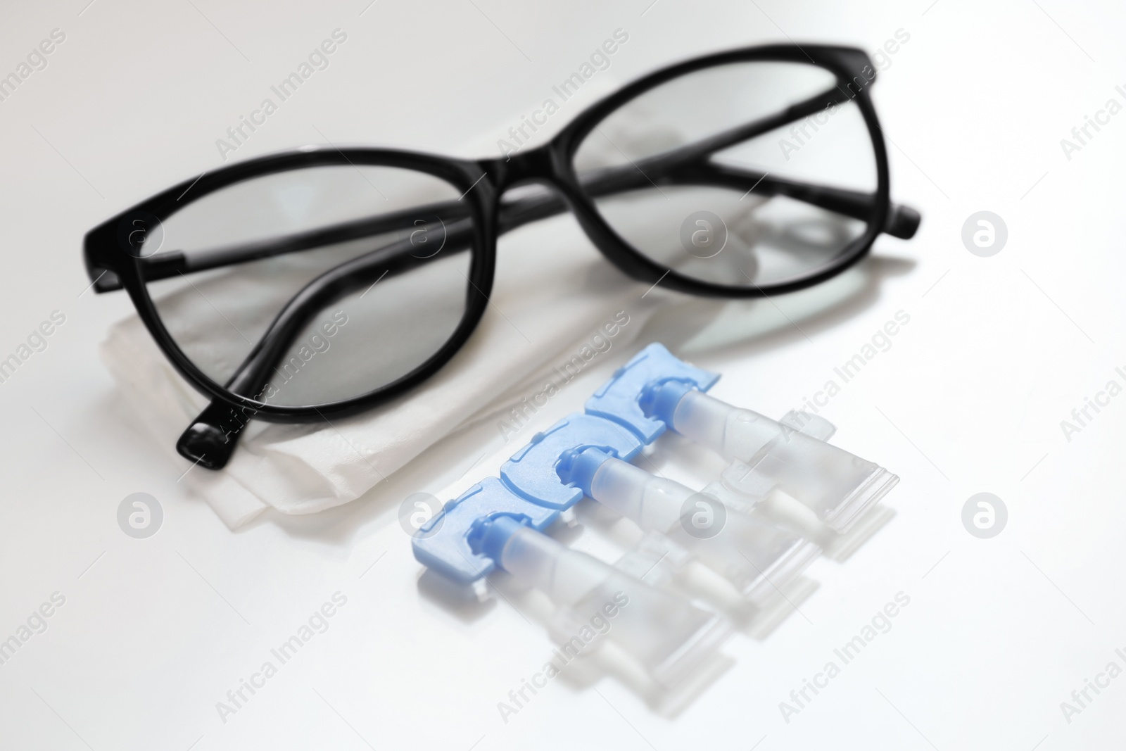 Photo of Single dose eye drops, glasses and fabric on white table