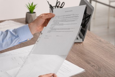 Businessman putting document into punched pocket at wooden table in office, closeup