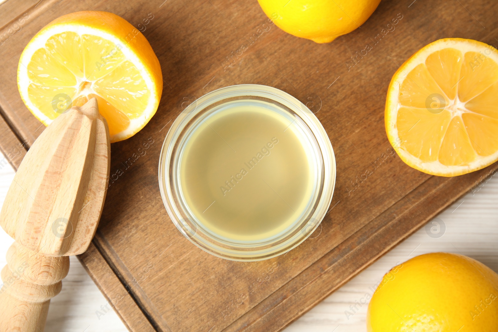 Photo of Freshly squeezed juice, lemons and reamer on wooden board, flat lay