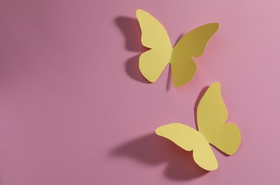 Photo of Yellow paper butterflies on pink background, top view. Space for text