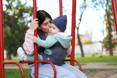 Photo of Mother holding her child in sling (baby carrier) on swing outdoors. Space for text