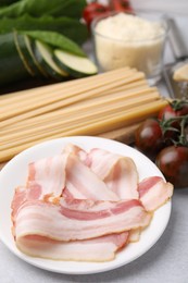 Photo of Raw pasta, bacon and fresh ingredients on light grey table