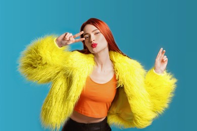 Stylish woman with red dyed hair blowing kiss on light blue background