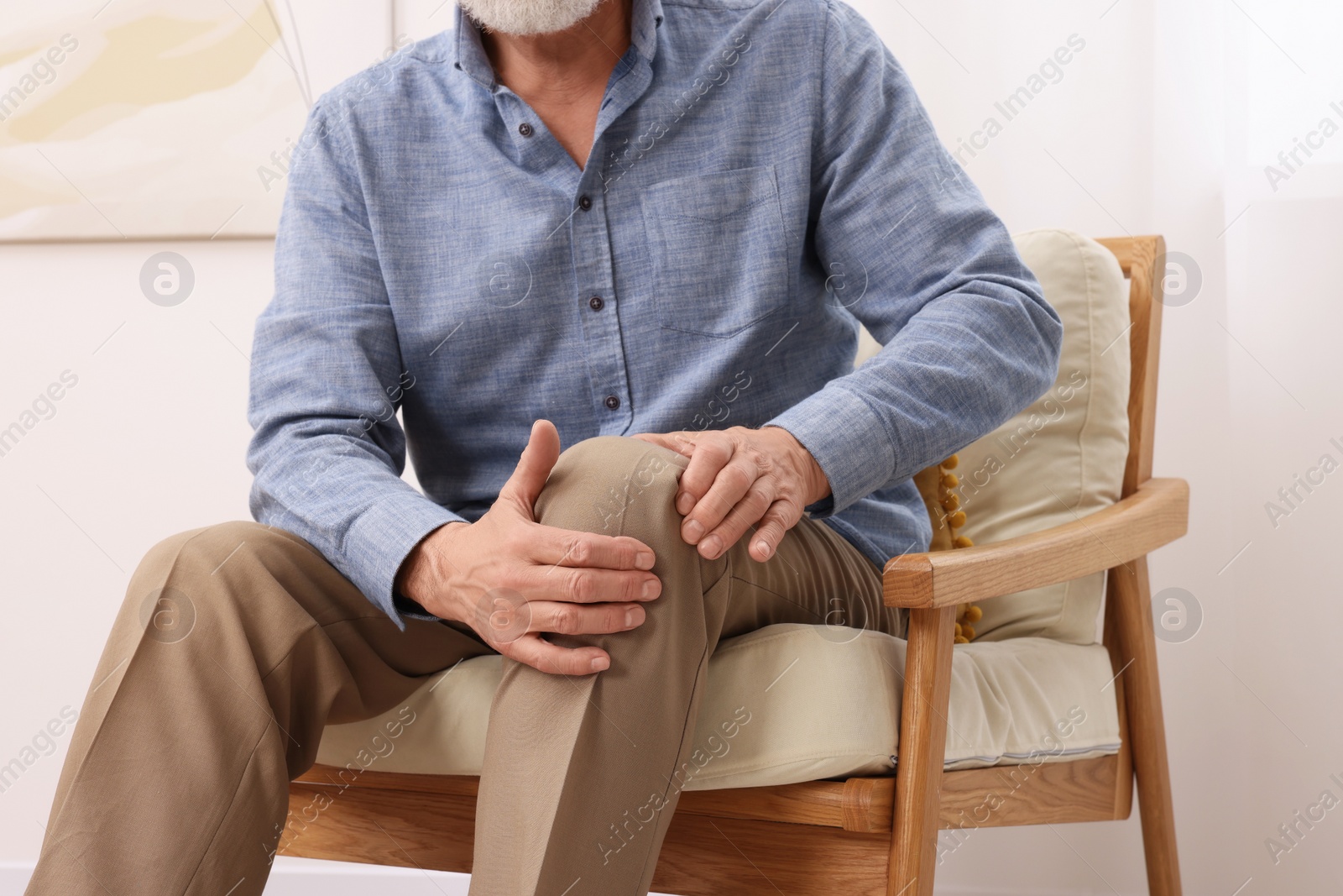 Photo of Senior man suffering from pain in his knee at home, closeup. Arthritis symptoms