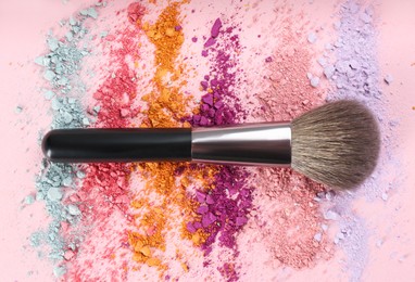 Makeup brush and scattered eye shadows on pink background, flat lay