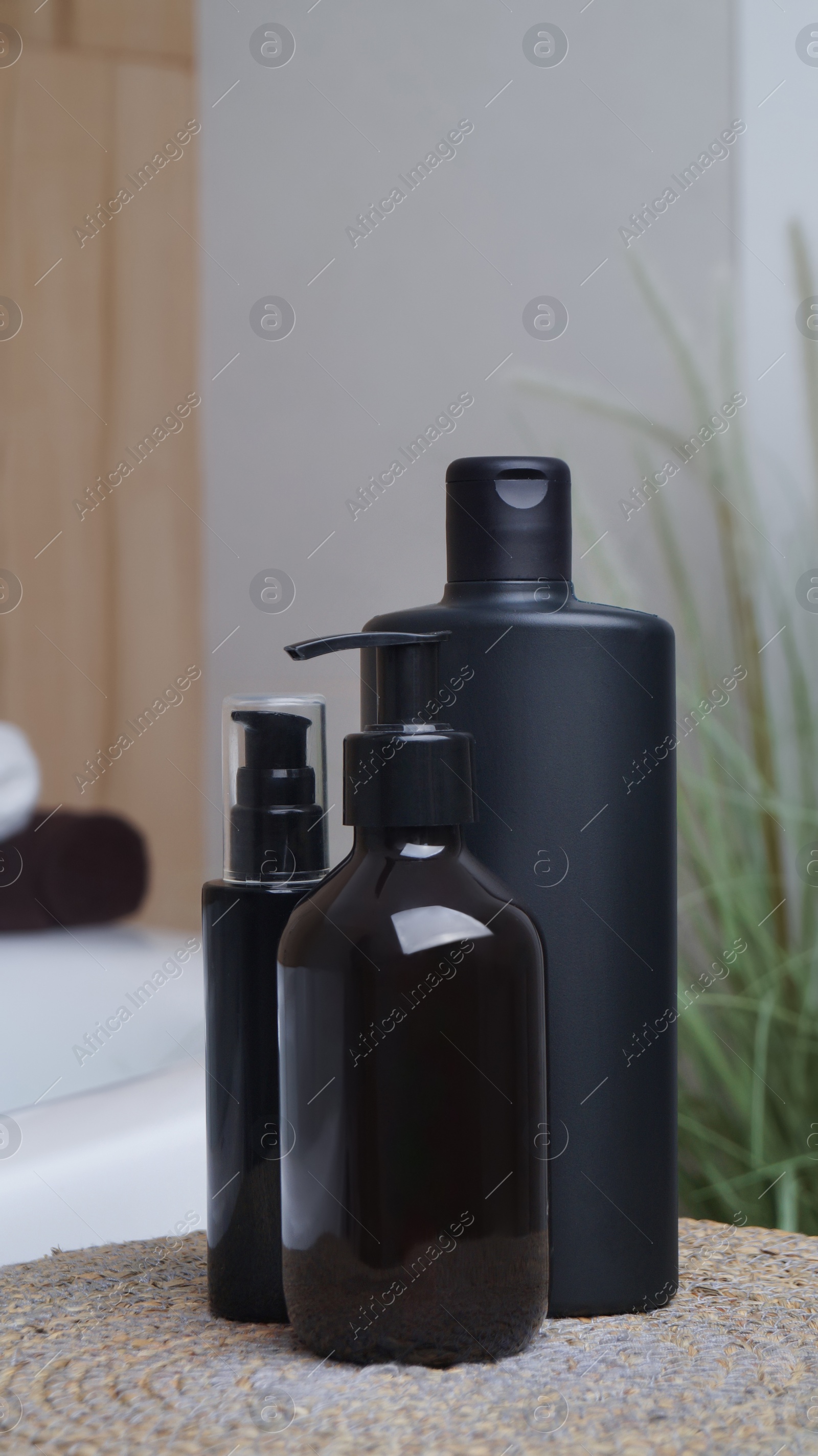 Photo of Bottle of bubble bath and cosmetic products on wicker mat near tub indoors