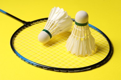 Photo of Feather badminton shuttlecocks and racket on yellow background, closeup