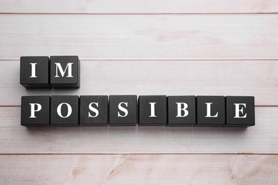 Photo of Motivation concept. Changing word from Impossible into Possible by removing black cubes on light wooden table, flat lay