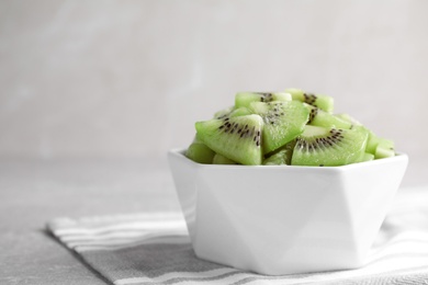 Photo of Bowl with kiwi slices on light grey table. Space for text