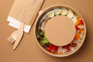 Photo of Tasty food in container with wooden fork and knife on beige background, flat lay. Space for text