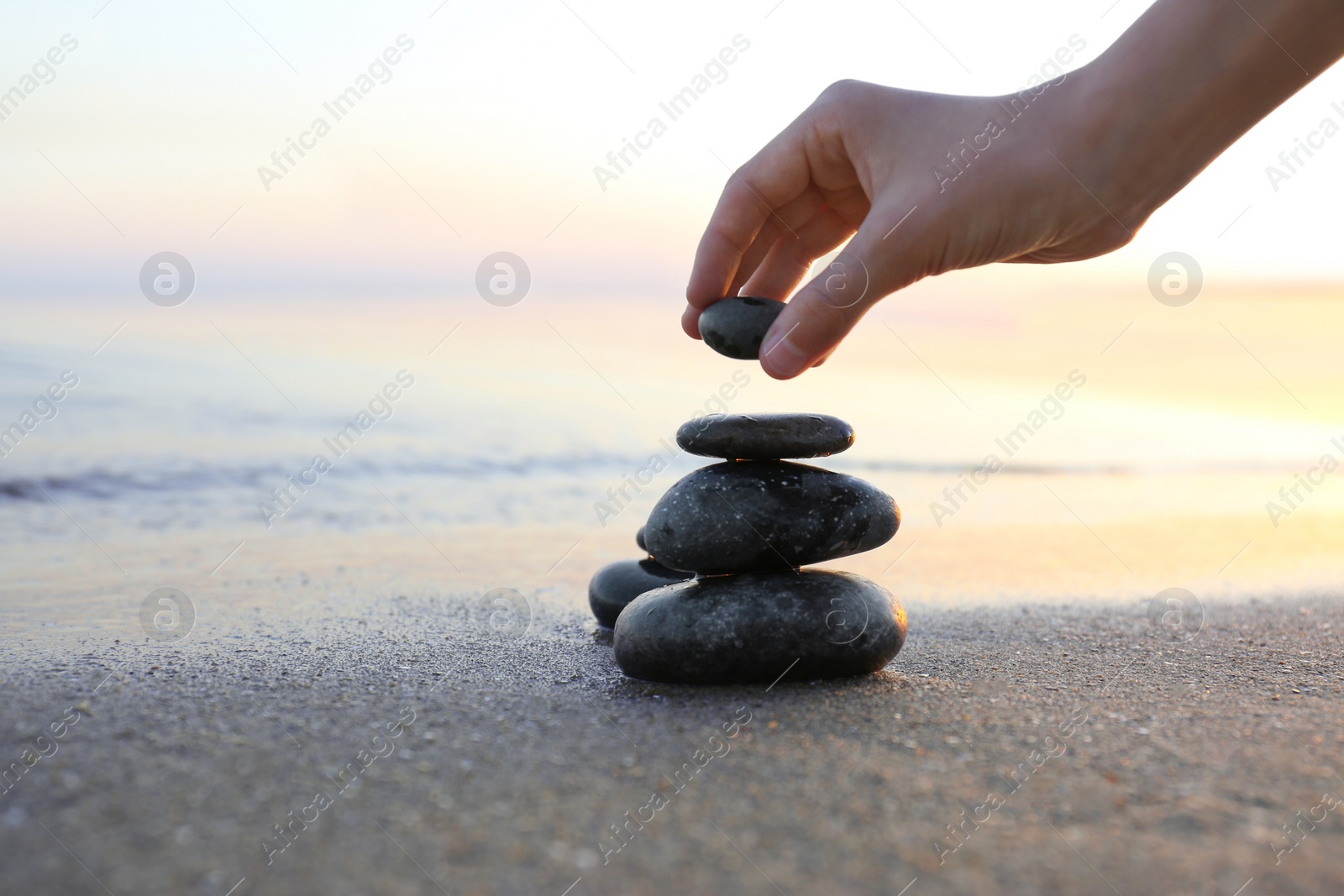 Photo of Woman stacking dark stones on sand near sea, space for text. Zen concept