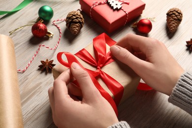 Photo of Woman decorating gift box at white wooden table, closeup. Christmas present