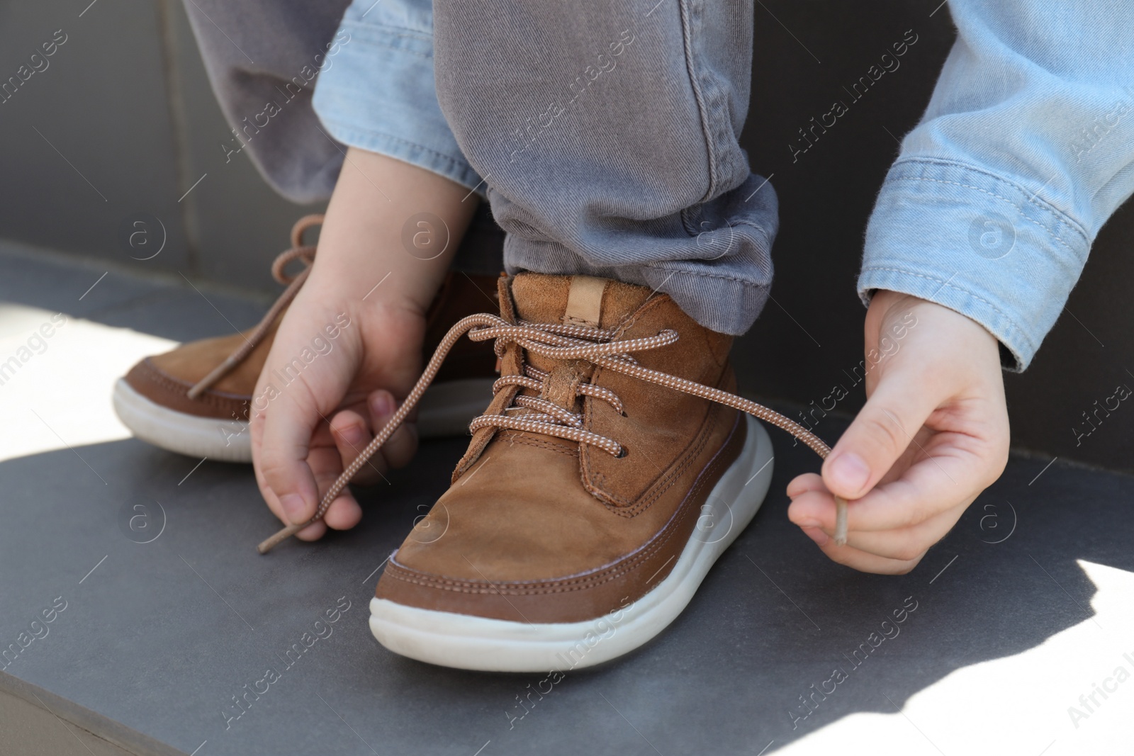 Photo of Little boy tying shoe laces on stairs outdoors, closeup