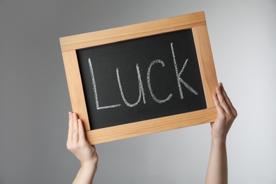 Woman holding blackboard with word LUCK on light grey background, closeup