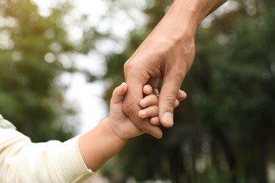 Photo of Daughter holding father's hand in park, closeup. Happy family
