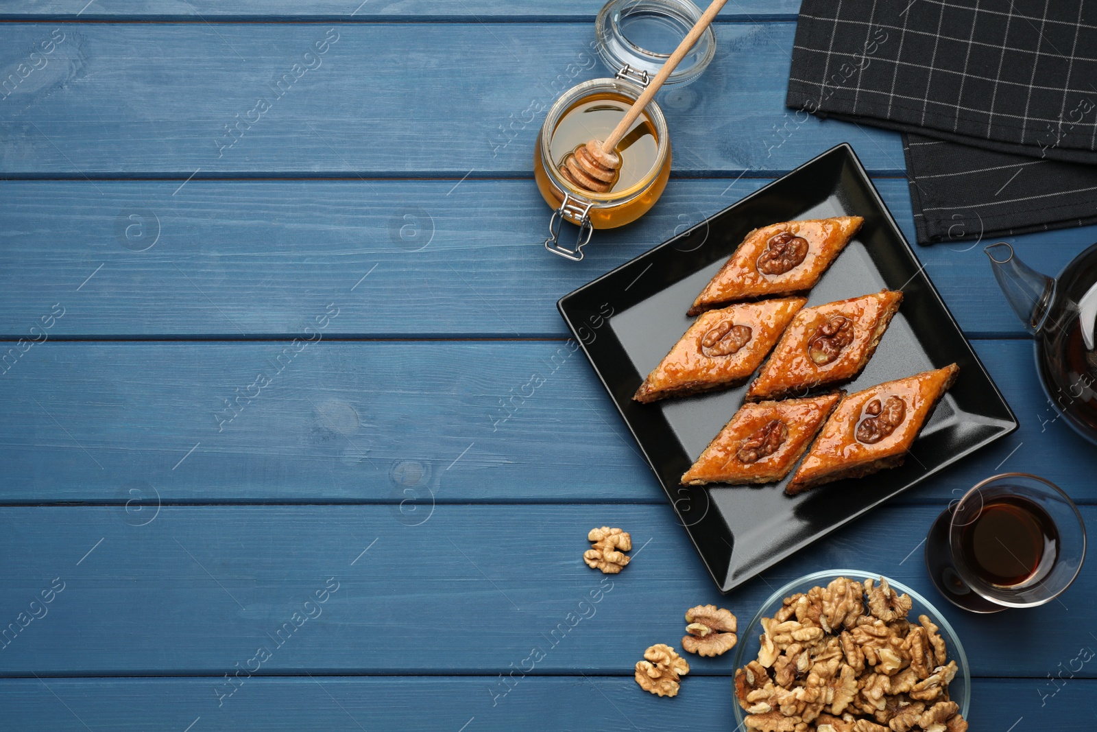 Photo of Delicious sweet baklava with walnuts, honey and hot tea on blue wooden table, flat lay. Space for text