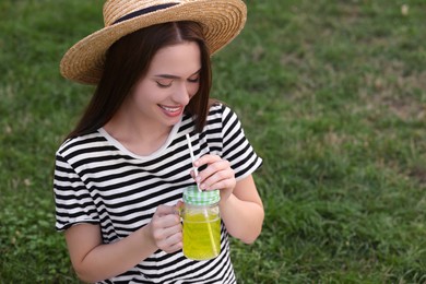 Photo of Young woman in straw hat with mason jar of fresh juice on green grass, space for text