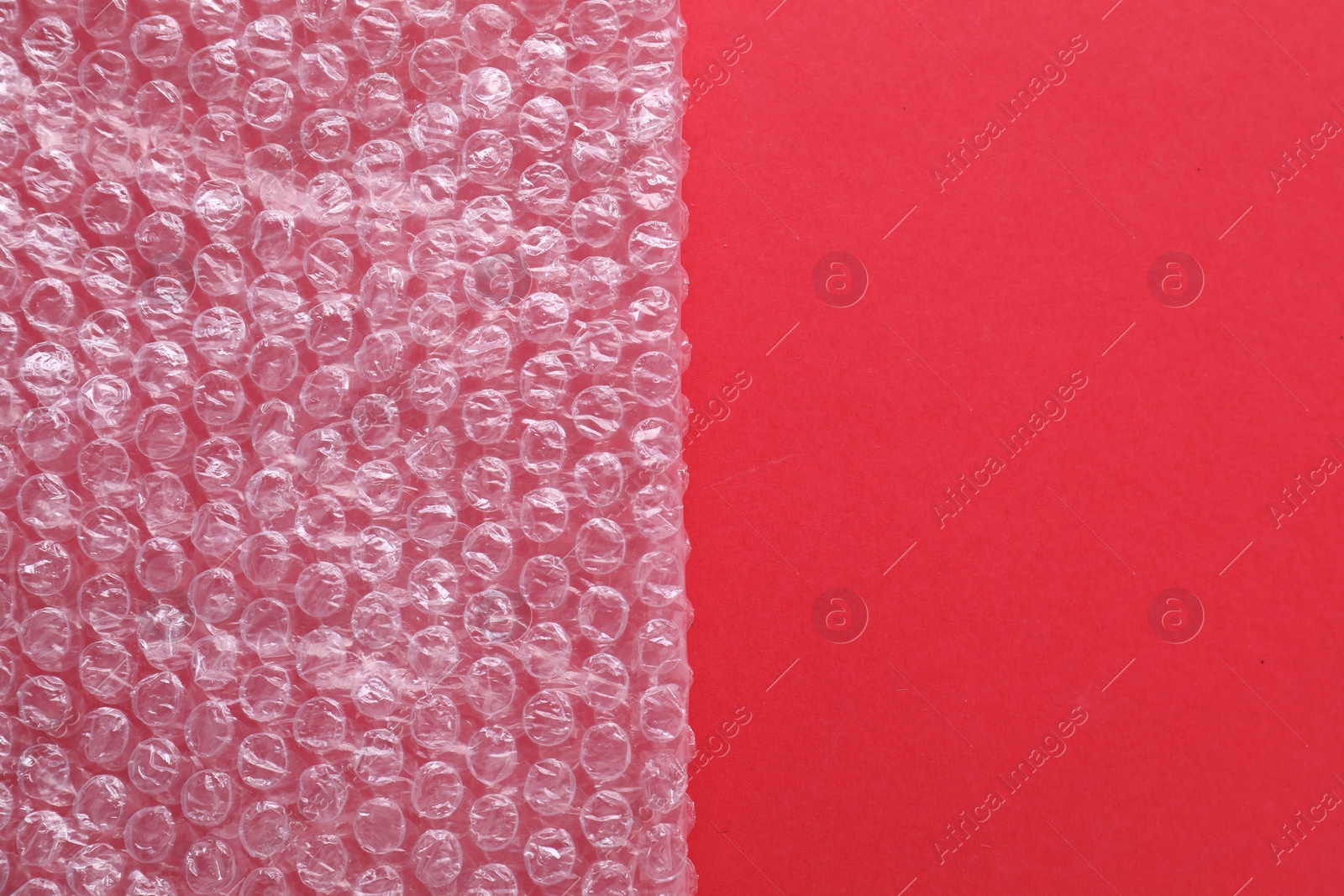 Photo of Transparent bubble wrap on red background, top view. Space for text