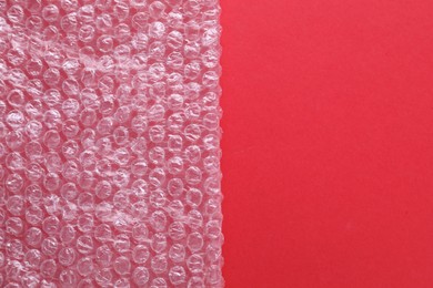 Photo of Transparent bubble wrap on red background, top view. Space for text