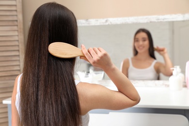 Photo of Beautiful young woman with hair brush looking into mirror in bathroom