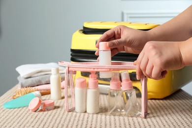 Photo of Woman putting small bottle with personal care product into plastic bag, closeup. Cosmetic travel kit