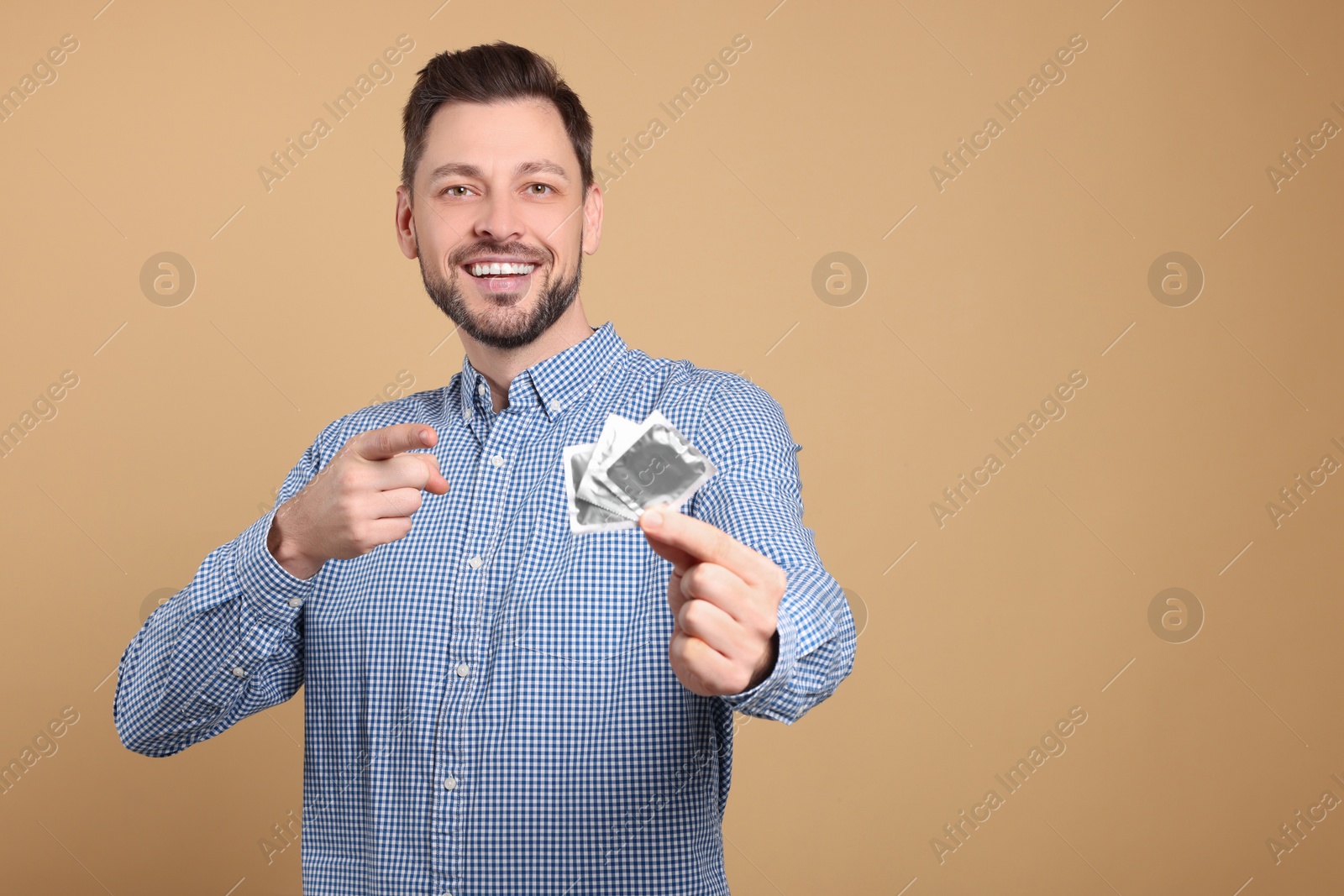 Photo of Happy man holding condoms on beige background. Space for text