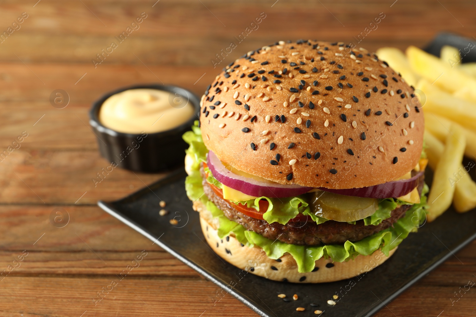 Burger with delicious patty, french fries and sauce on wooden table, closeup Photo of Burger with delicious patty, french fries and sauce on wooden table, closeup