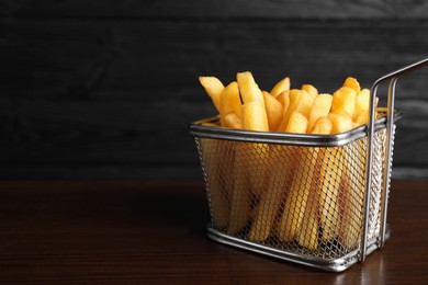 Photo of Frying basket with tasty french fries on wooden table, closeup. Space for text
