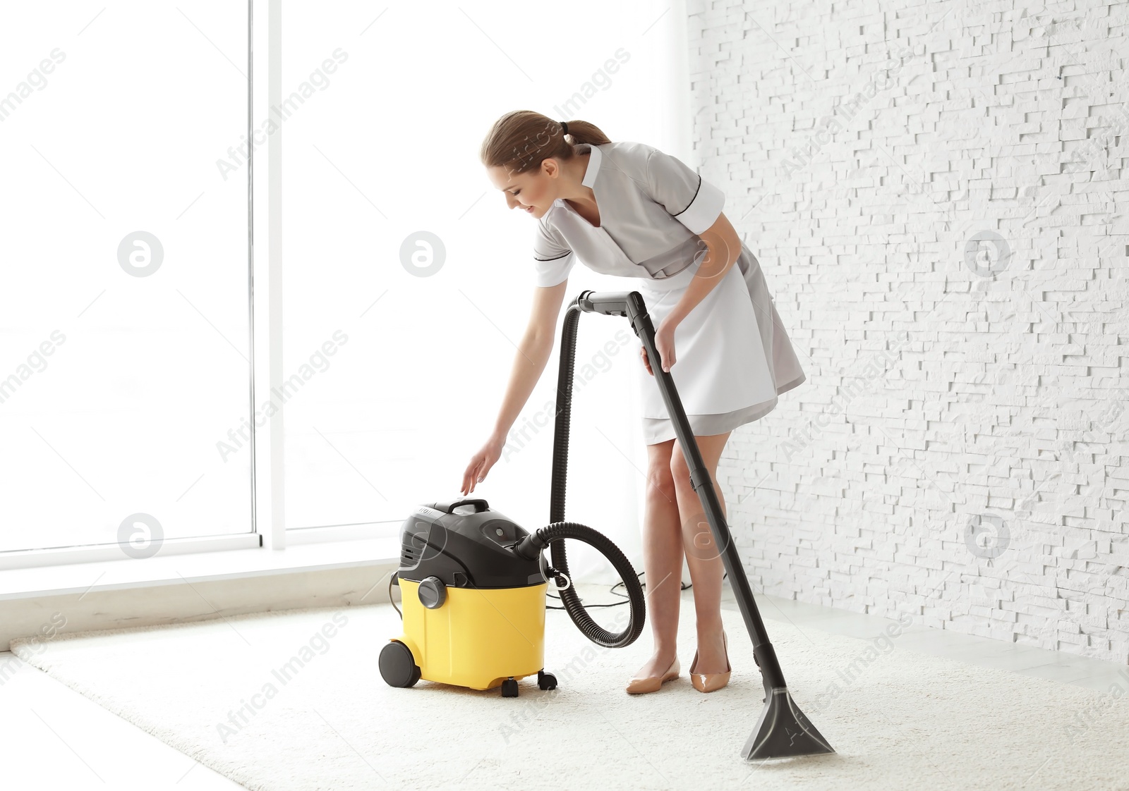 Photo of Chambermaid cleaning carpet with vacuum  indoors