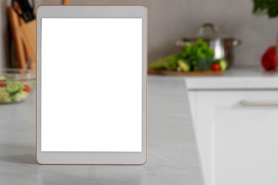 Photo of Modern tablet with blank screen on white marble table in kitchen, space for text