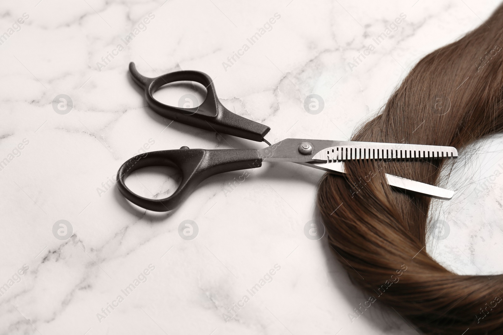 Photo of Professional hairdresser scissors and strand of brown hair on marble background