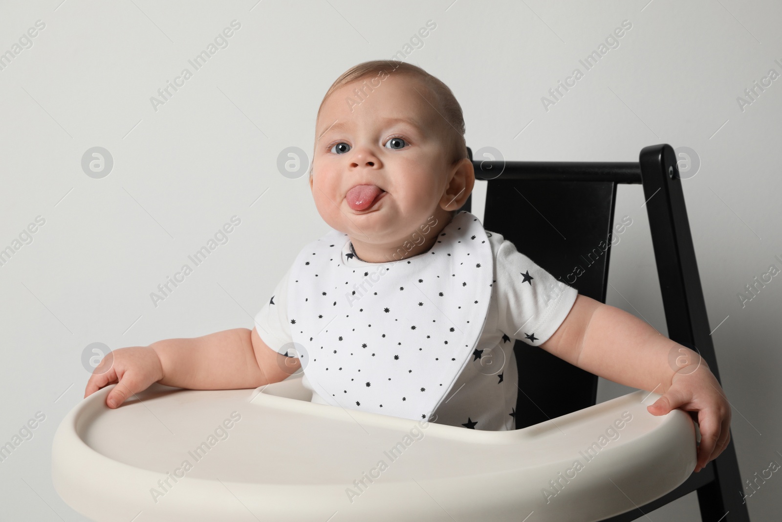 Photo of Cute little baby wearing bib in highchair on white background