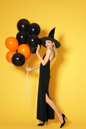 Photo of Beautiful woman wearing witch costume with balloons for Halloween party on yellow background