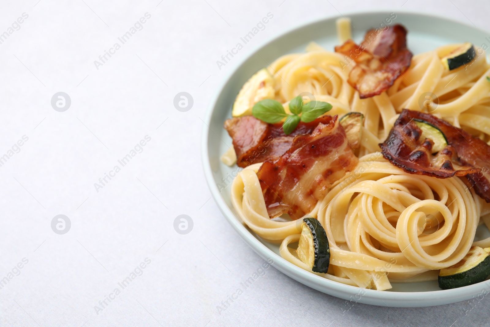 Photo of Tasty pasta with bacon and basil on white table, closeup. Space for text