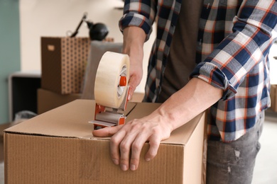 Photo of Young man packing moving box indoors, closeup