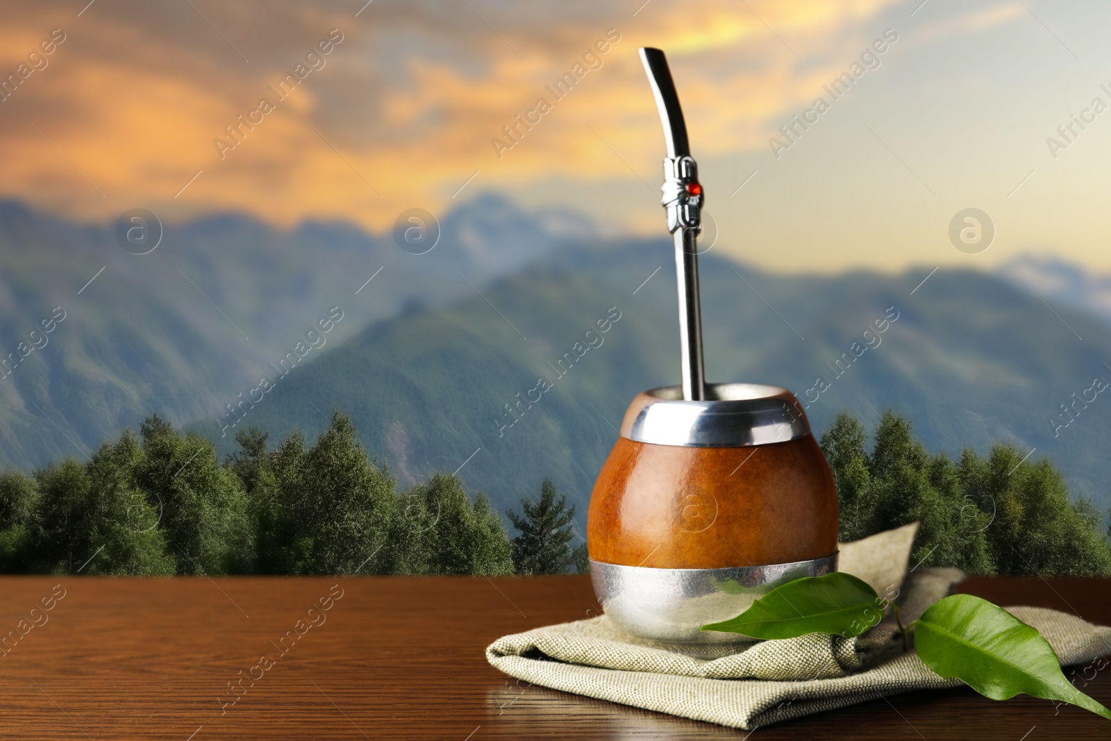 Image of Calabash with mate tea and bombilla on wooden table outdoors at sunset. Space for text