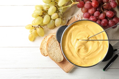 Flat lay composition with pot of delicious cheese fondue on wooden table