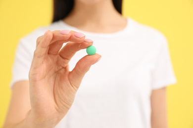 Photo of Young woman with vitamin pill on yellow background, closeup