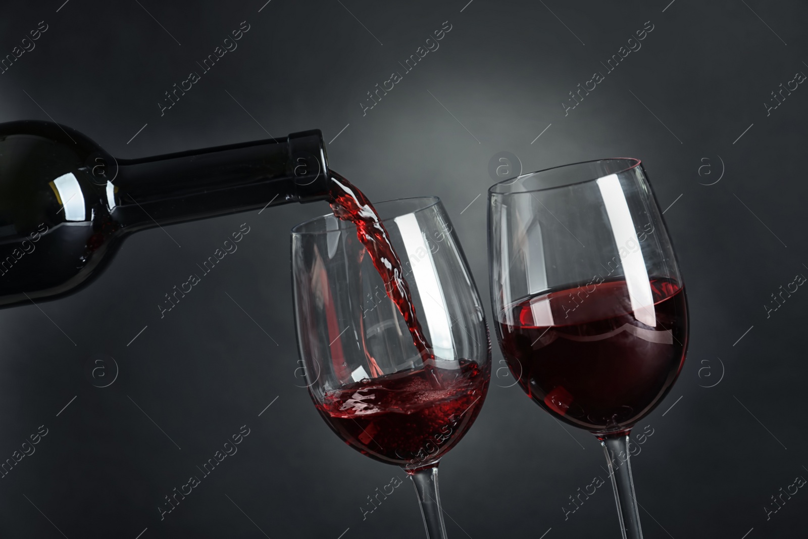 Photo of Pouring delicious red wine into glass on dark background