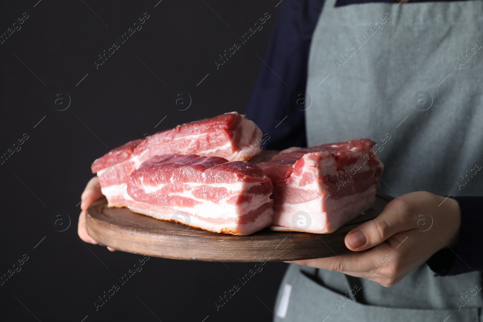 Photo of Woman holding wooden board with pieces of raw pork belly on black background, closeup