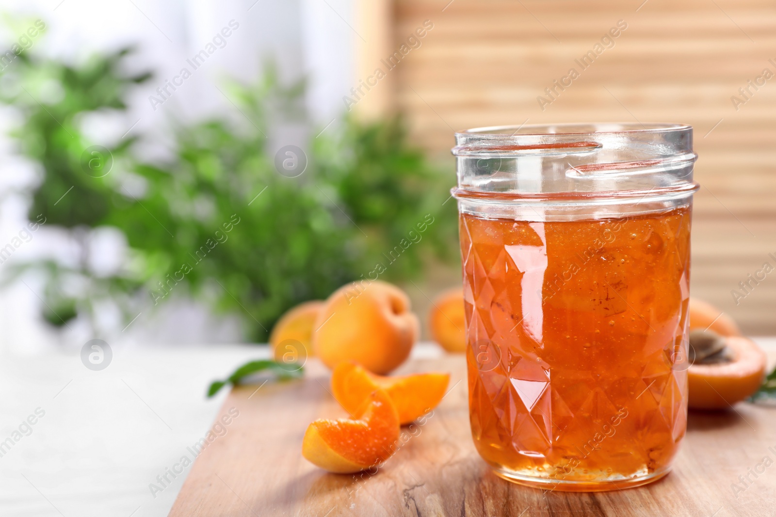 Photo of Jar with tasty apricot jam on wooden board