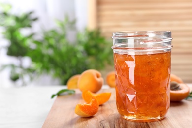 Photo of Jar with tasty apricot jam on wooden board