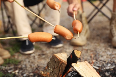 Photo of People frying sausages on bonfire outdoors. Camping season